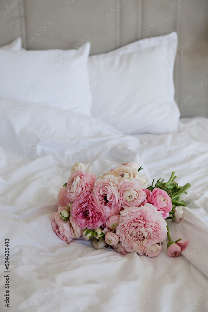 A beautiful bouquet of peonies and ranunculus flowers on the empty unmade bed with white sheets. A r