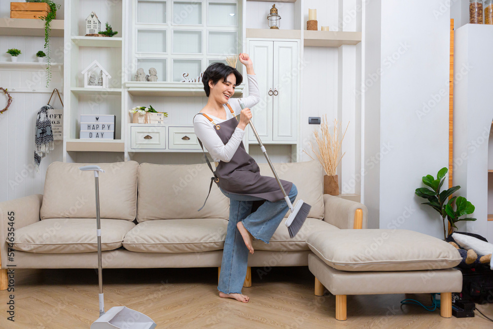 Full length shot of cheerful young woman, cleaning lady pretending to sing a song with holding broom