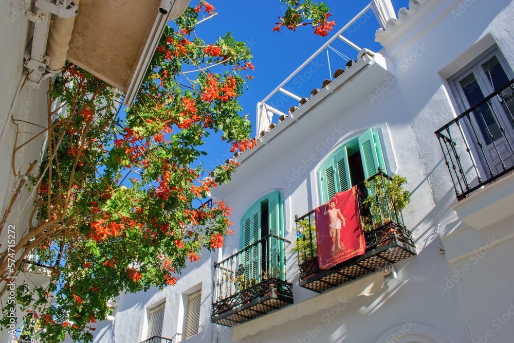 Street of famous white spanish village Frigiliana with symbol of religious patron San Sebastian - An