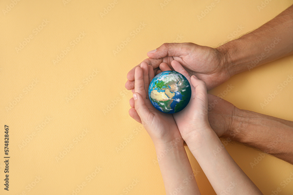 Hands of father and child holding small planet Earth on beige background