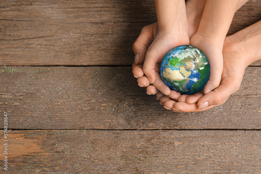 Hands of mother and child holding small planet Earth on wooden background