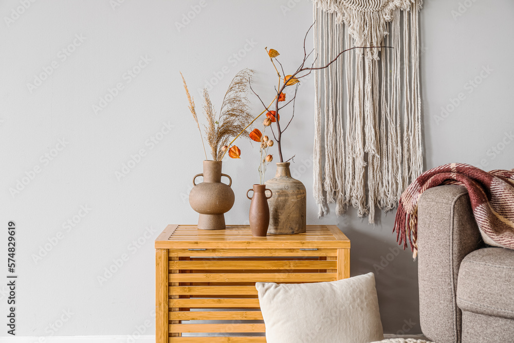 Vases with tree branches, flowers and pampas grass on table near light wall