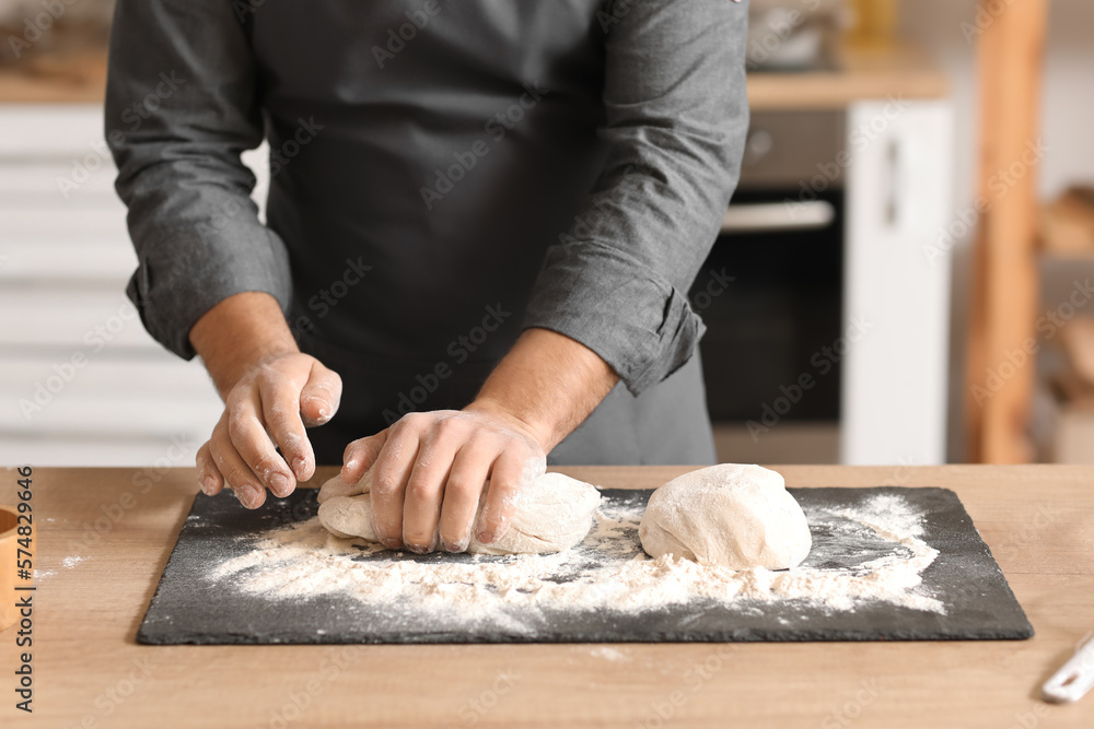 Male baker preparing dough at table in kitchen, closeup