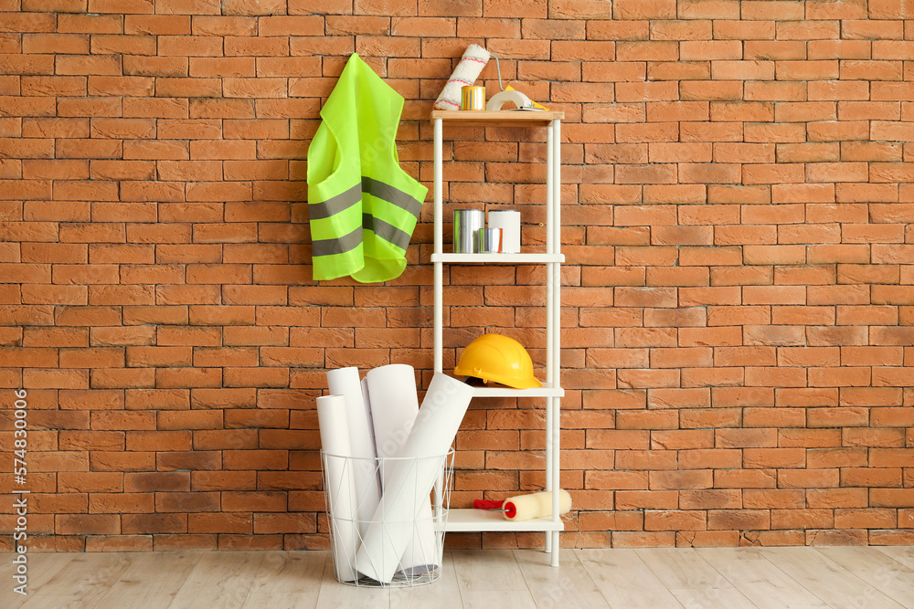 Safety vest, shelving unit with renovation supplies and hardhat near brick wall