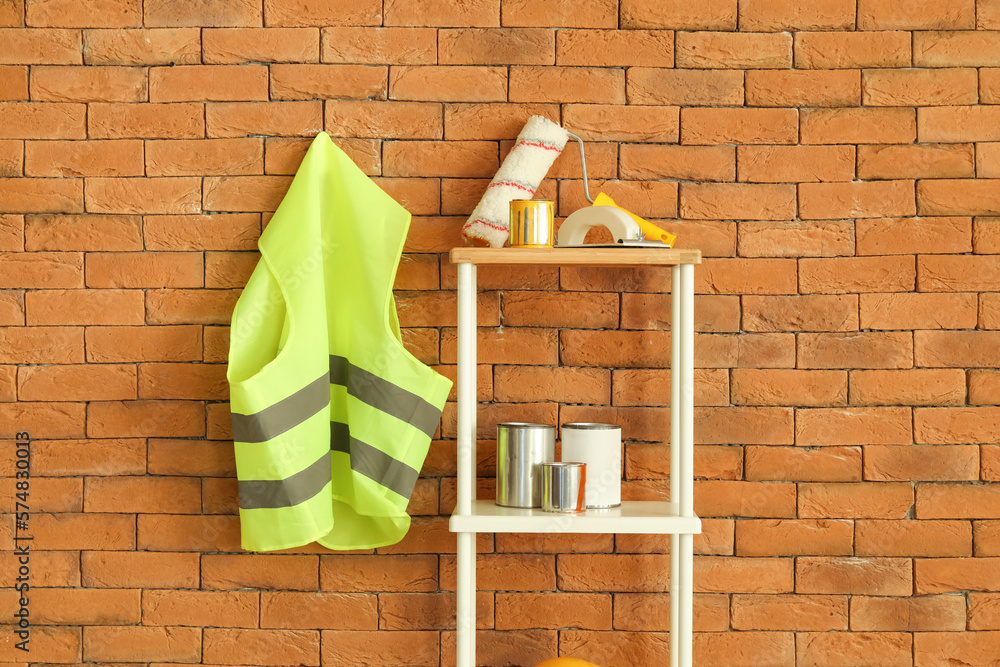 Safety vest and shelving unit with renovation supplies near brick wall