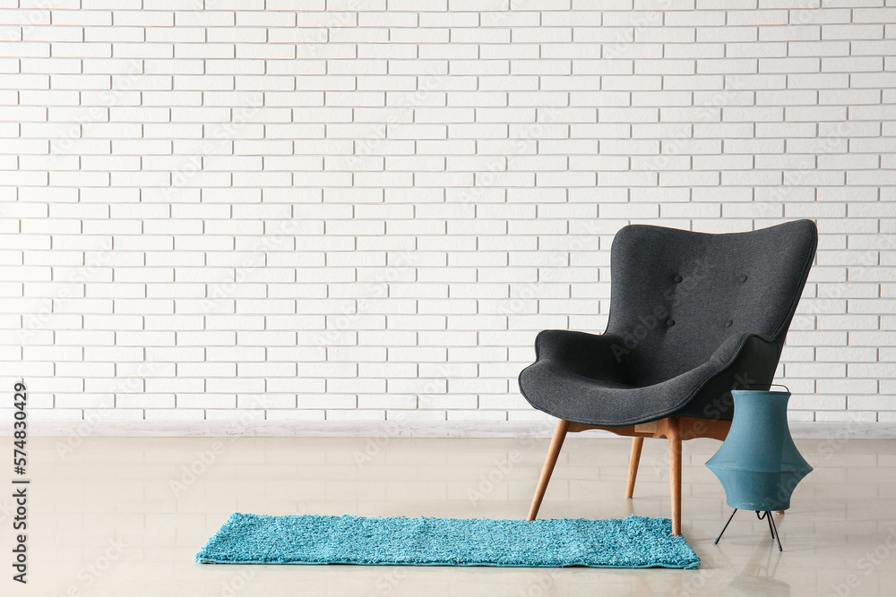 Stylish grey armchair, lantern and blue rug near white brick wall