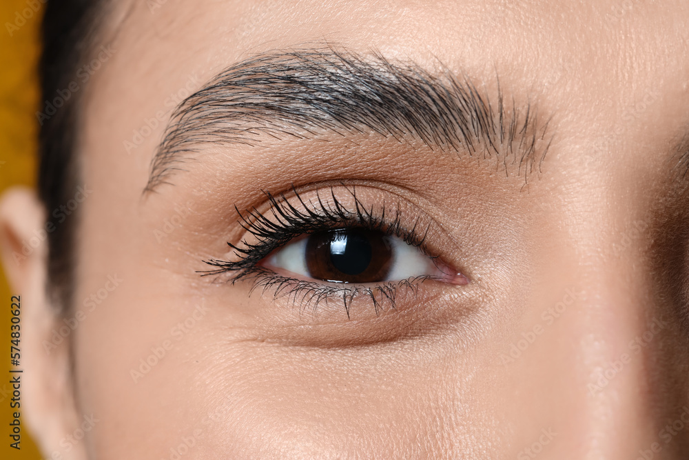 Woman with brown eyes on yellow background, closeup