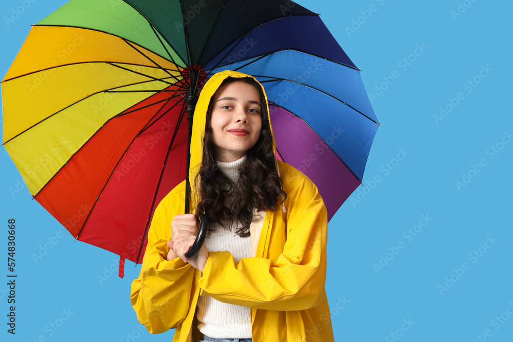 Teenage girl in raincoat with umbrella on blue background