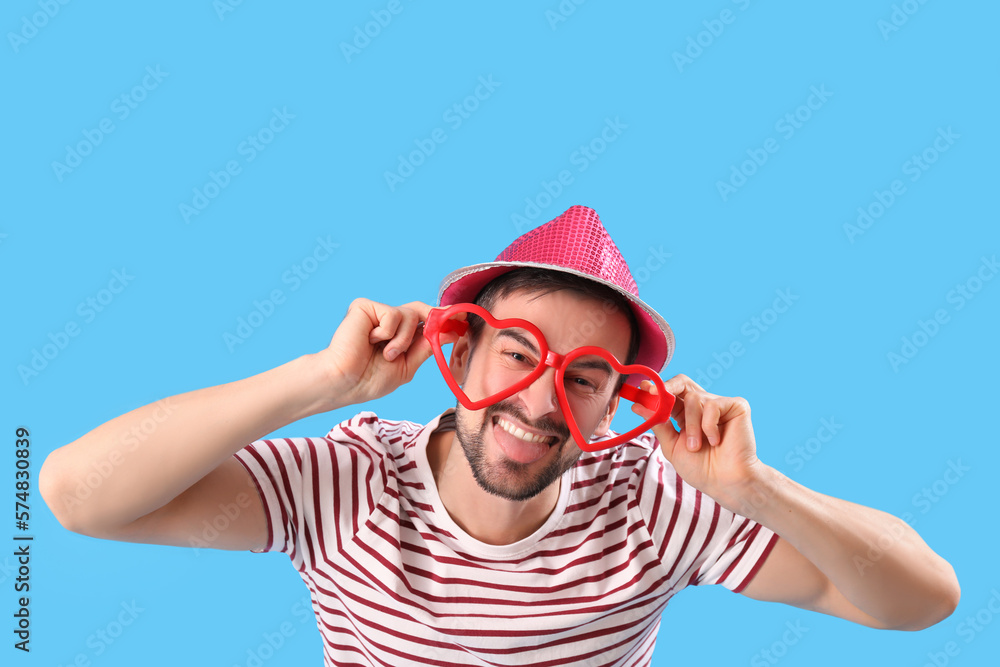 Funny young man in eyeglasses on blue background. April Fools Day celebration