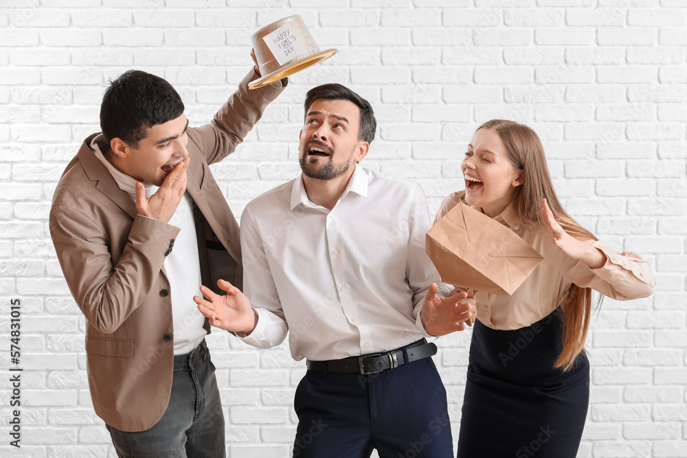 Business people playing a prank on their colleague against white brick background. April Fools Day 