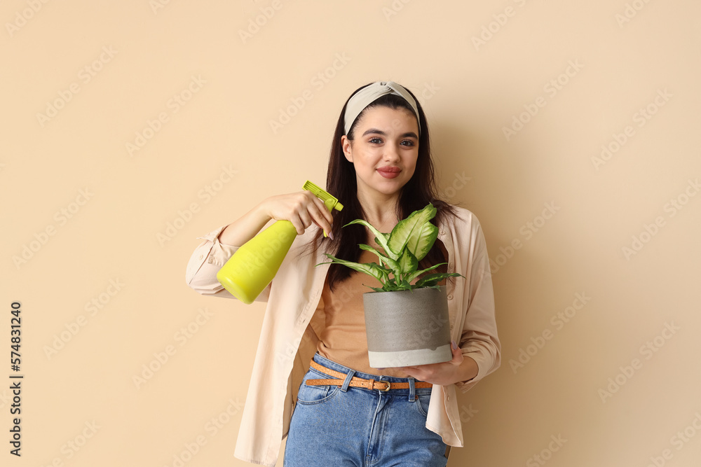 Young woman with spray bottle and green houseplant on beige background