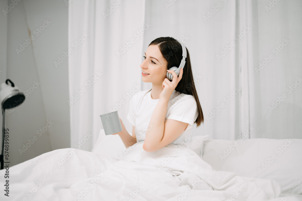 Beautiful young woman on a white bed with coffee cub and using smart phone at home. lifestyle concep