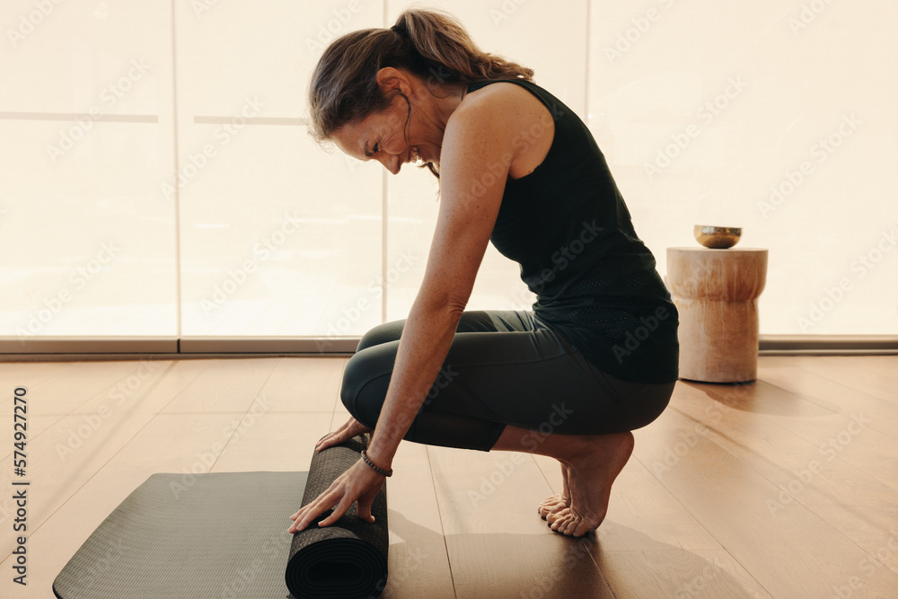 Cheerful senior woman folding up a yoga mat at home