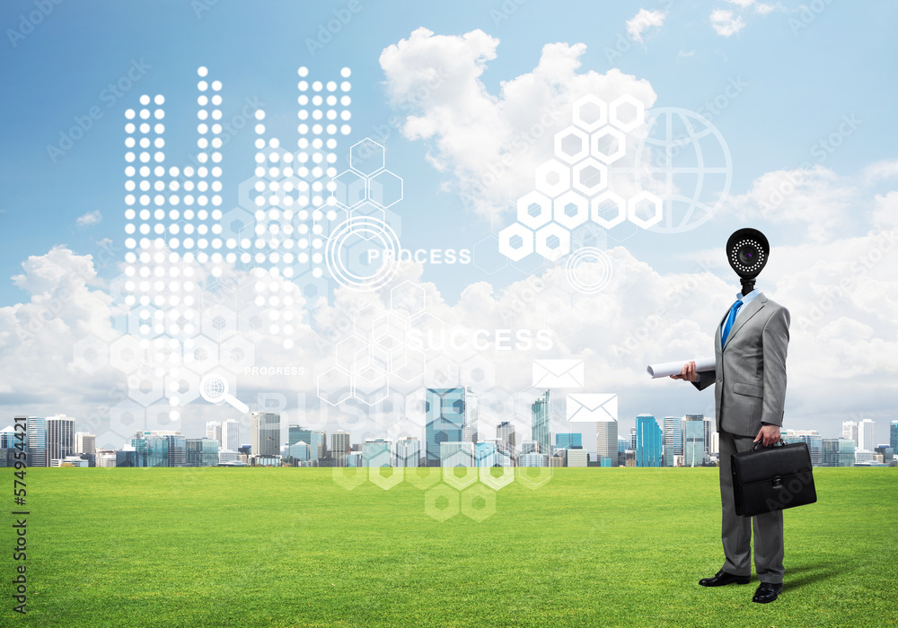 Camera headed man standing on green grass against modern cityscape