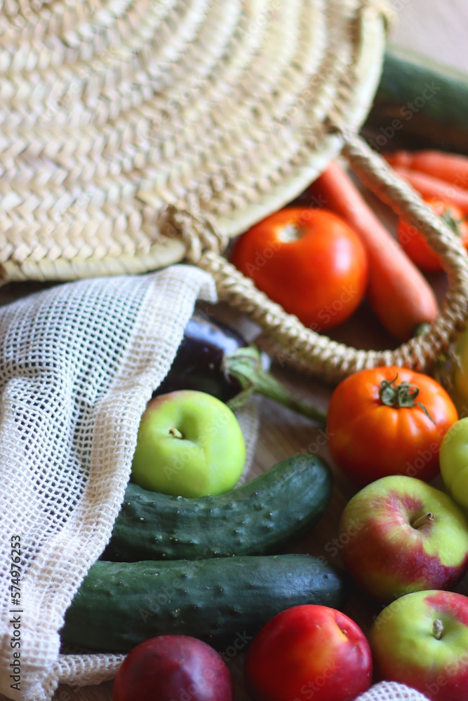 Straw bag and reusable fabric bags filled with various healthy fruit and vegetables. Wooden backgrou