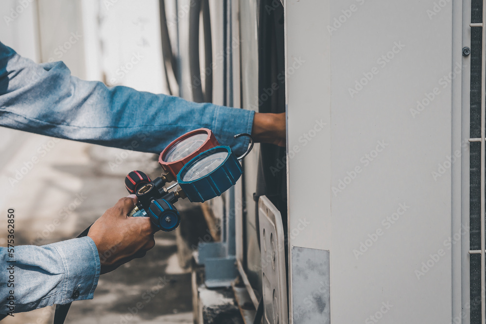 Air repair mechanic using measuring equipment for filling industrial factory air conditioners and ch