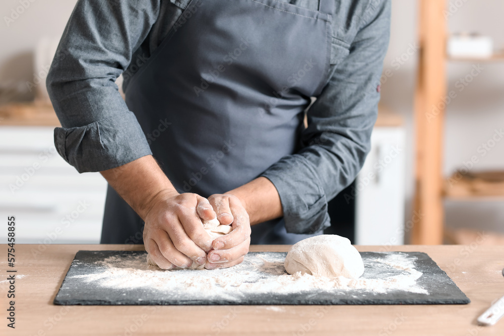 Male baker preparing dough at table in kitchen, closeup