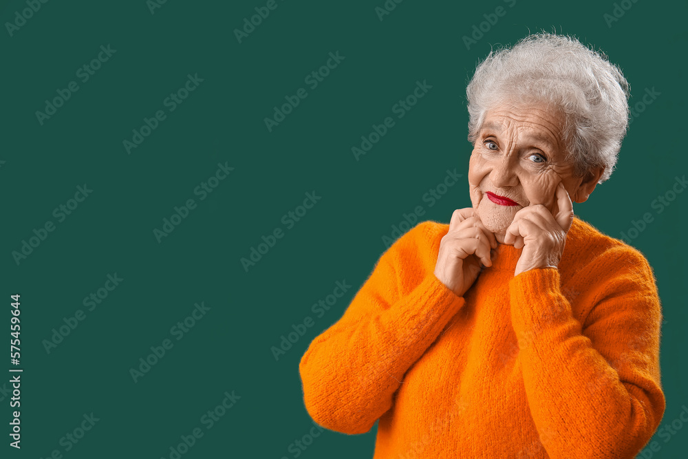 Senior woman in orange sweater on green background