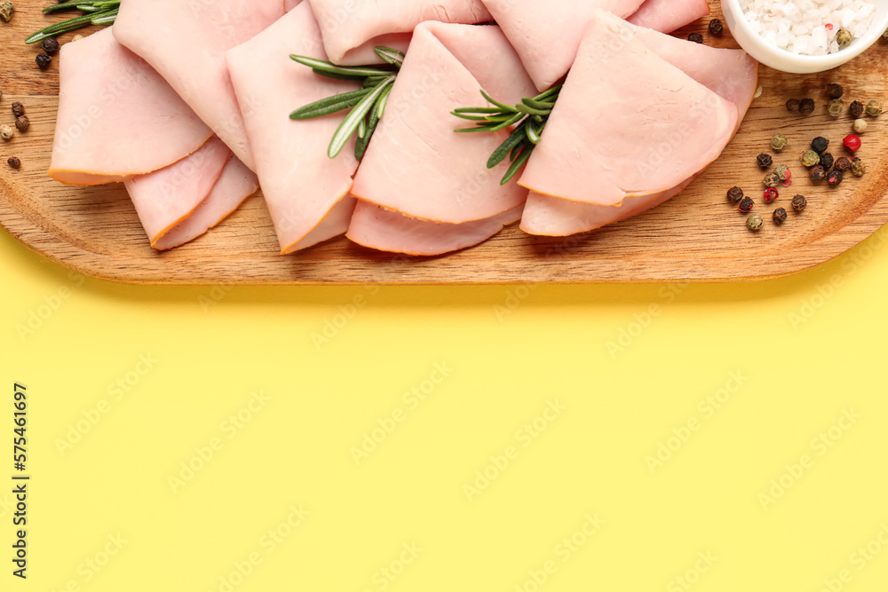 Board with slices of tasty ham, rosemary and peppercorn on yellow background