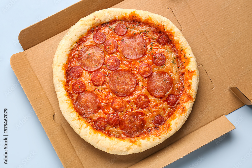 Cardboard box with delicious pepperoni pizza on blue background