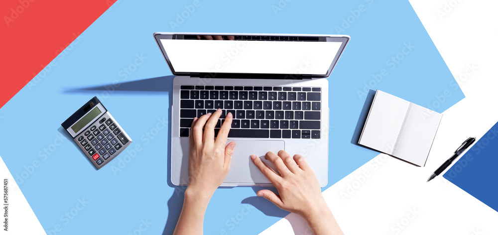 Person using a laptop computer with a notebook and a calculator - flat lay