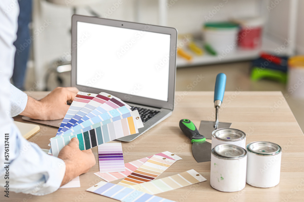 Male painter with color palettes using laptop at table in room, closeup