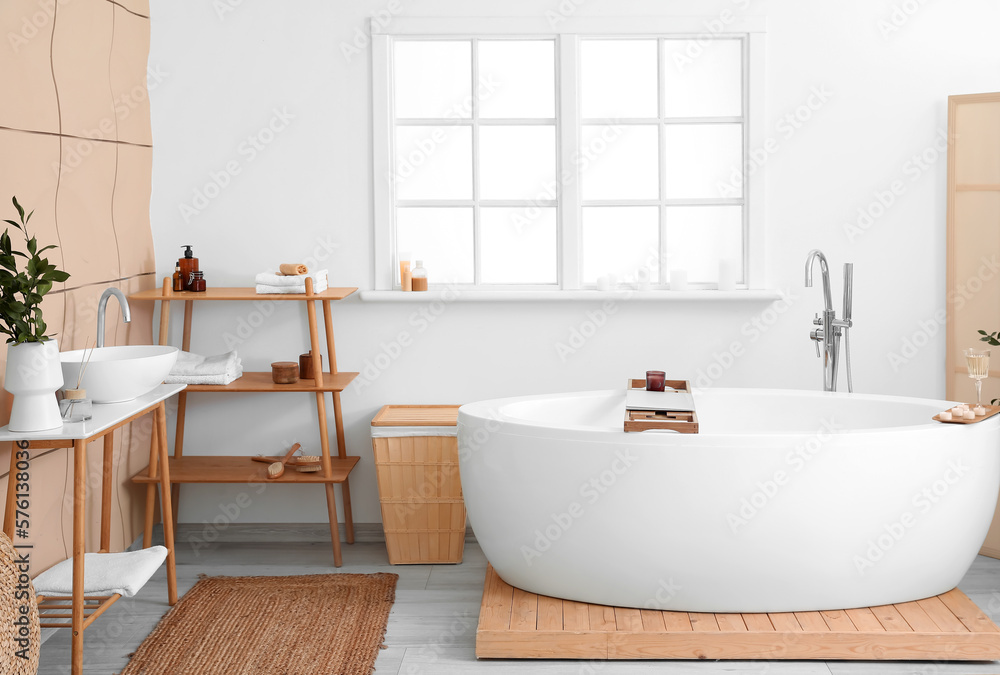 Interior of bathroom with modern bathtub, laptop, champagne and burning candles on board