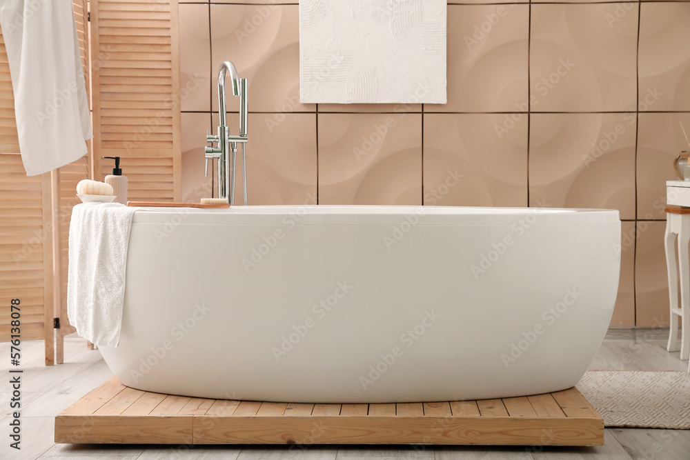 Interior of bathroom with modern bathtub, folding screen and towels