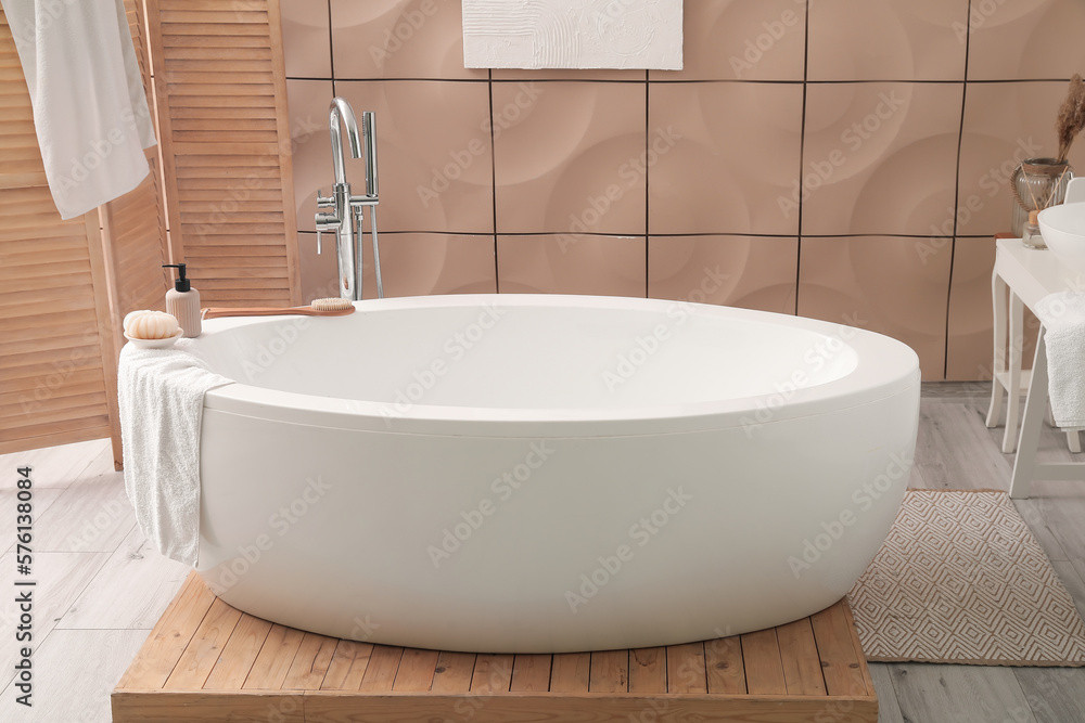 Interior of bathroom with modern bathtub, folding screen and towels