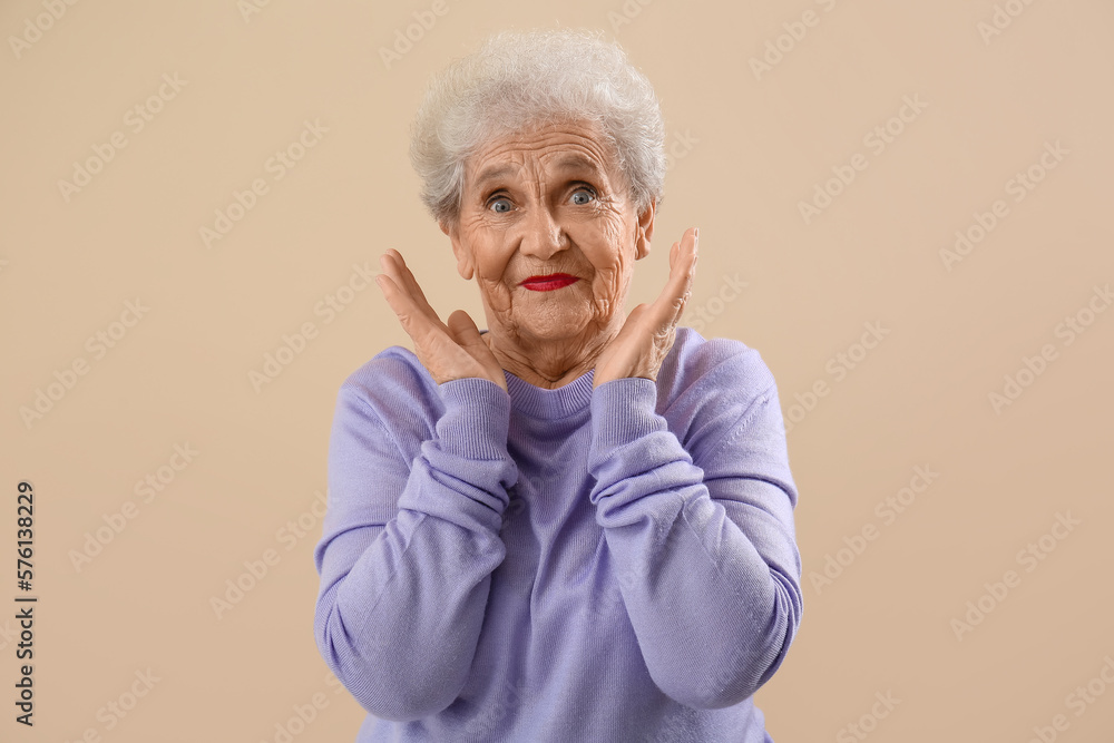 Surprised senior woman in lilac sweater on beige background