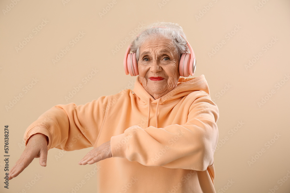 Senior woman in headphones dancing on beige background