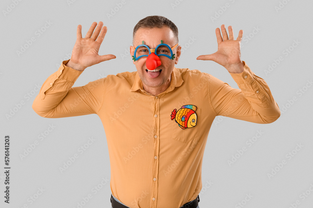 Mature man in funny disguise on grey background. April Fools Day celebration