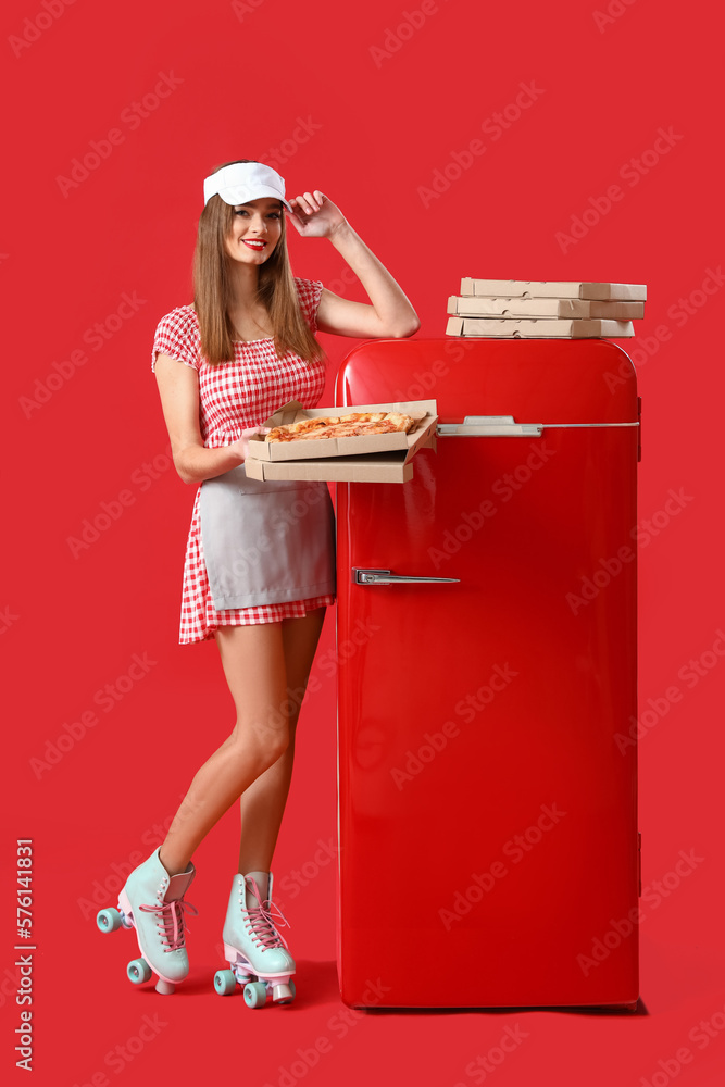 Young woman in roller skates with tasty pizza and fridge on red background