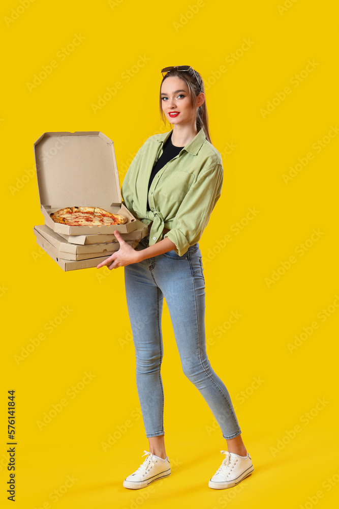 Young woman with cardboard boxes of tasty pizza on yellow background