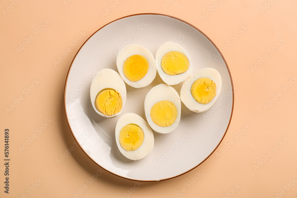 Plate with halves of delicious boiled eggs on beige background