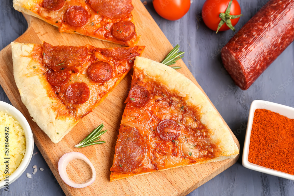 Board with slices of delicious pepperoni pizza and ingredients on blue wooden background