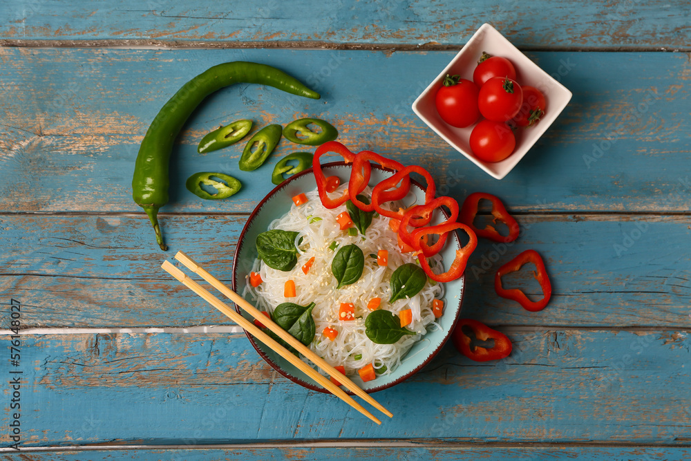 Composition with bowl of tasty rice noodles and vegetables on color wooden background