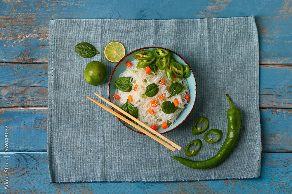 Composition with bowl of tasty rice noodles, chili pepper and lime on color wooden background