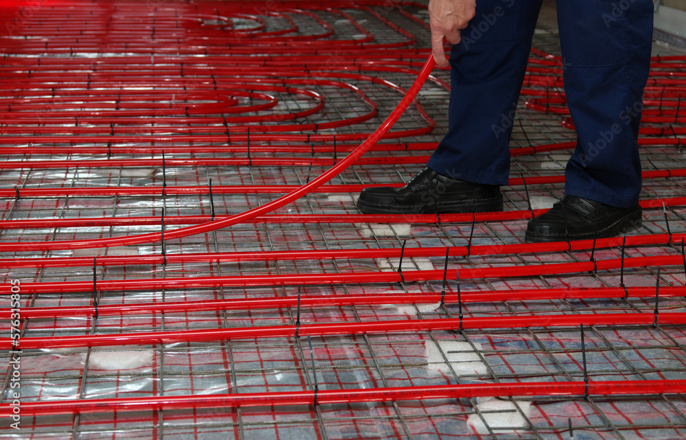 Worker is installing a red pipe for underfloor heating