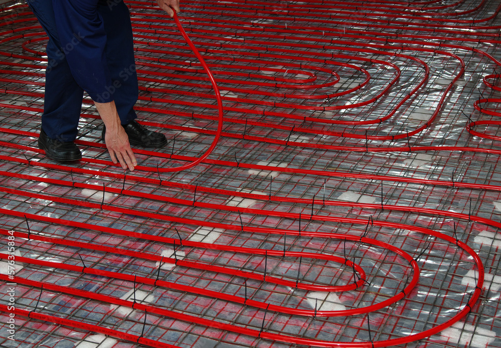 Worker is installing a red pipe for underfloor heating