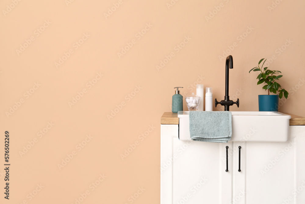 Table with sink, bath accessories and houseplant near beige wall