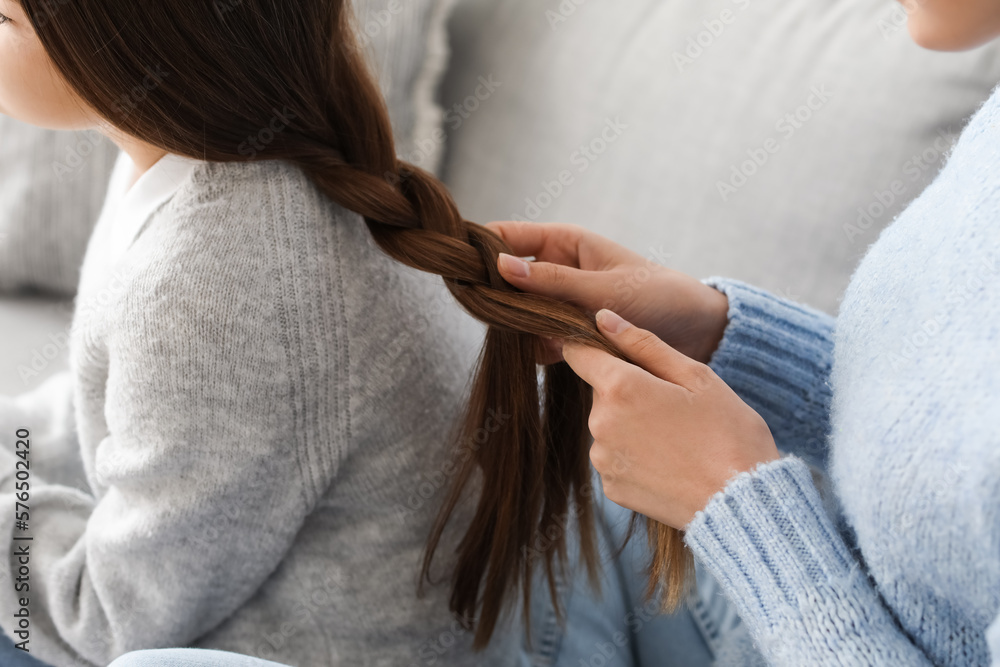 Mother doing hair of her little daughter at home, closeup