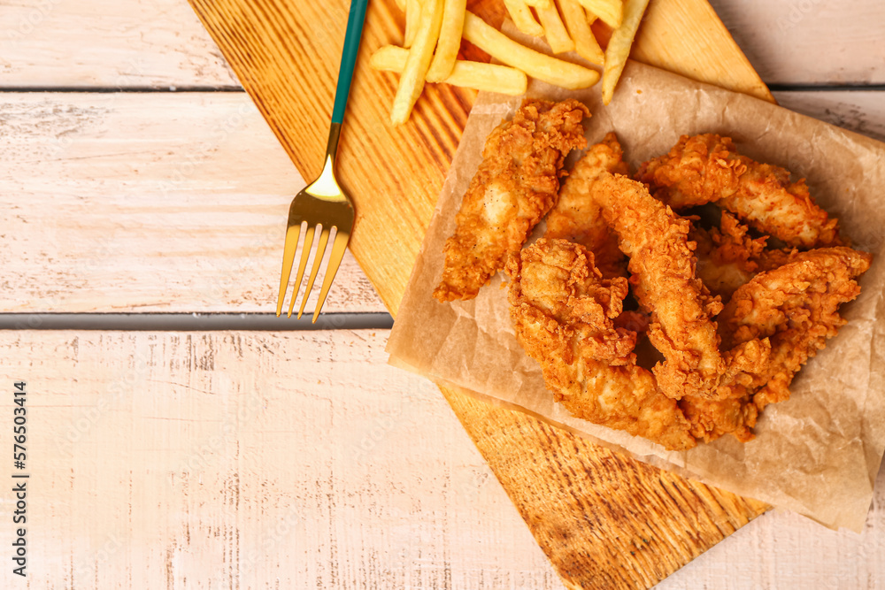 Board with tasty nuggets and french fries on light wooden background