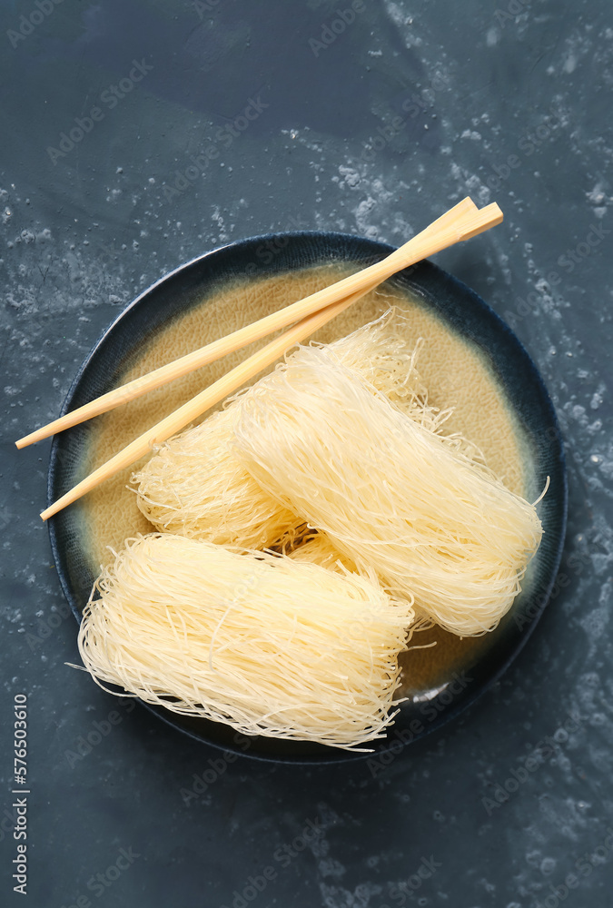 Plate with raw rice noodles and chopsticks on dark background