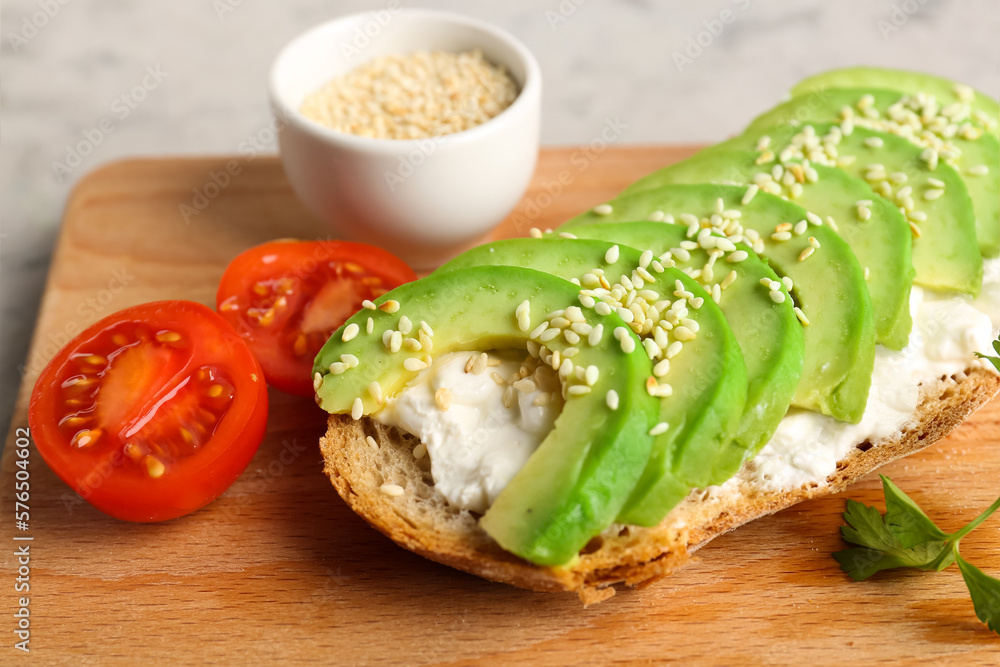 Board with delicious avocado toast and sesame seeds on grey background