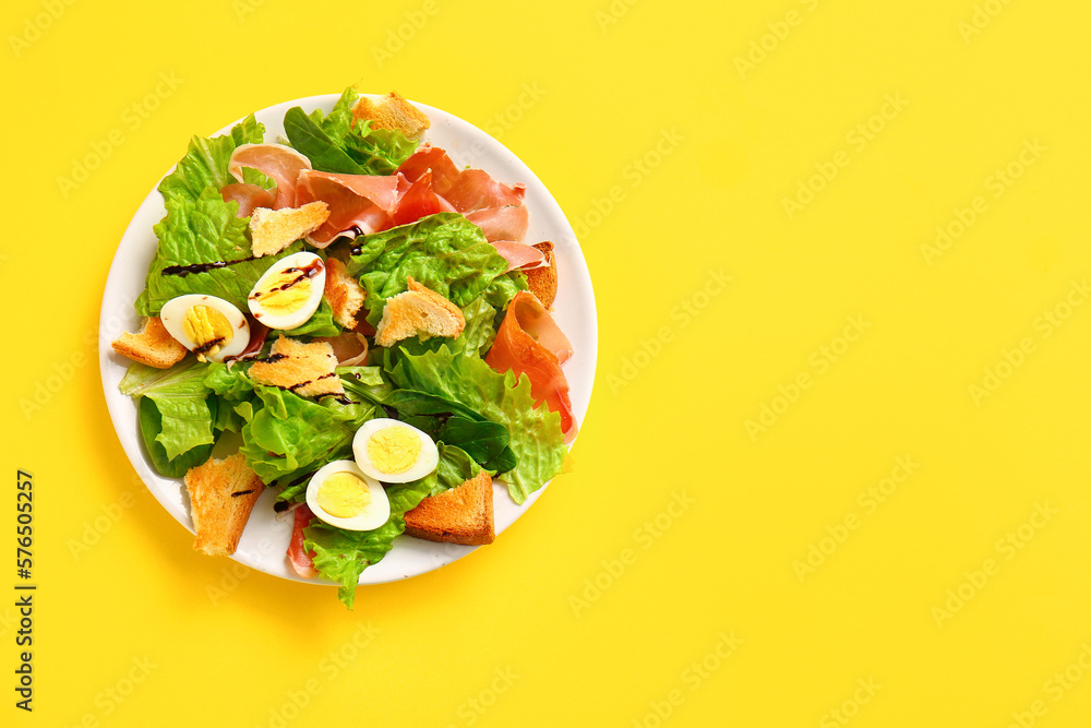 Plate of delicious salad with boiled eggs and jamon on yellow background