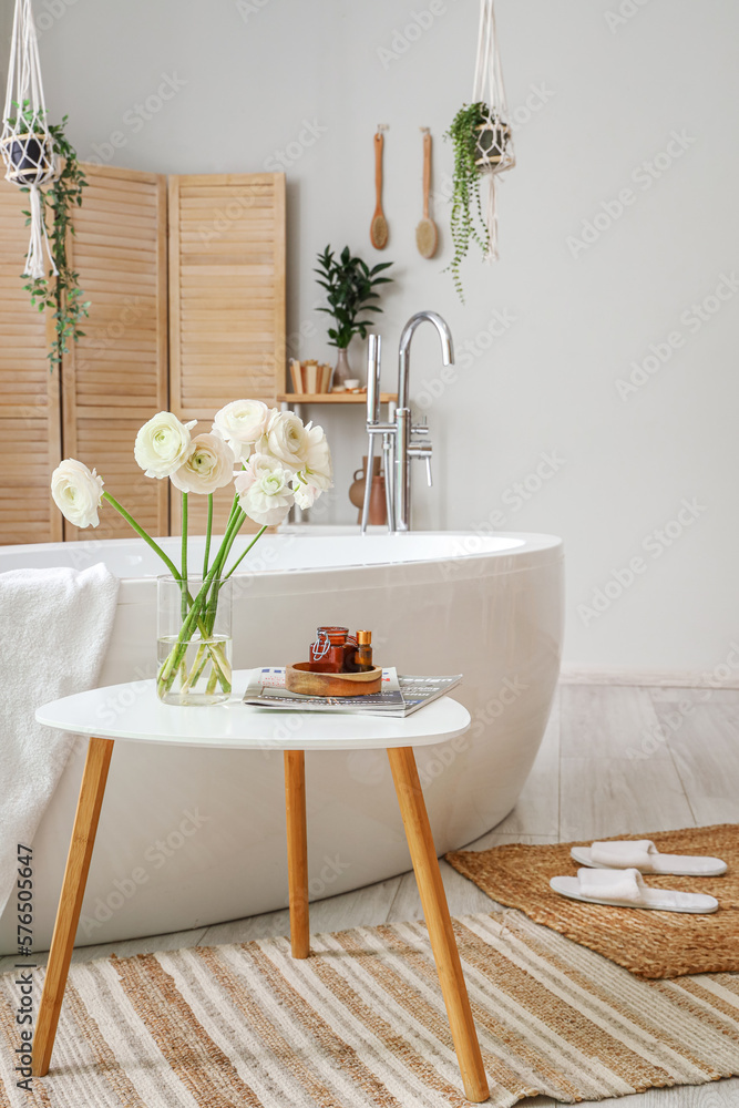 Vase with ranunculus flowers and magazines on table in bathroom