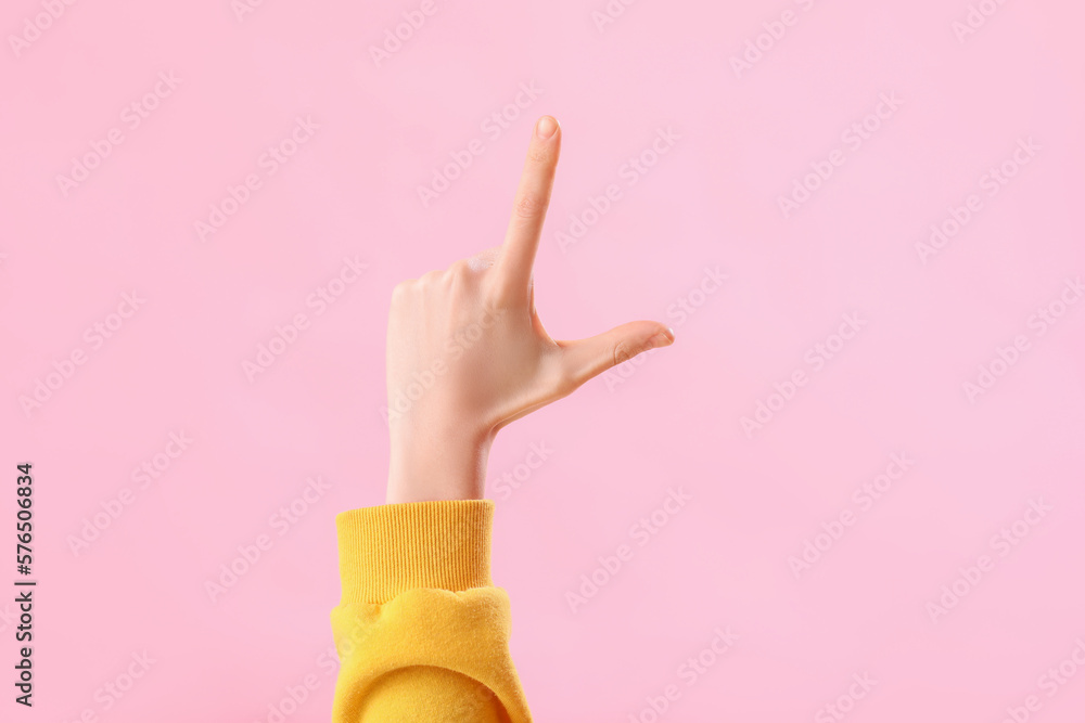 Young woman showing loser gesture on pink background