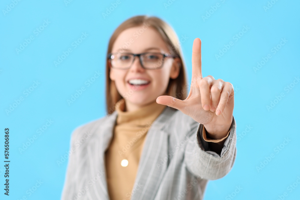 Young businesswoman showing loser gesture on blue background, closeup