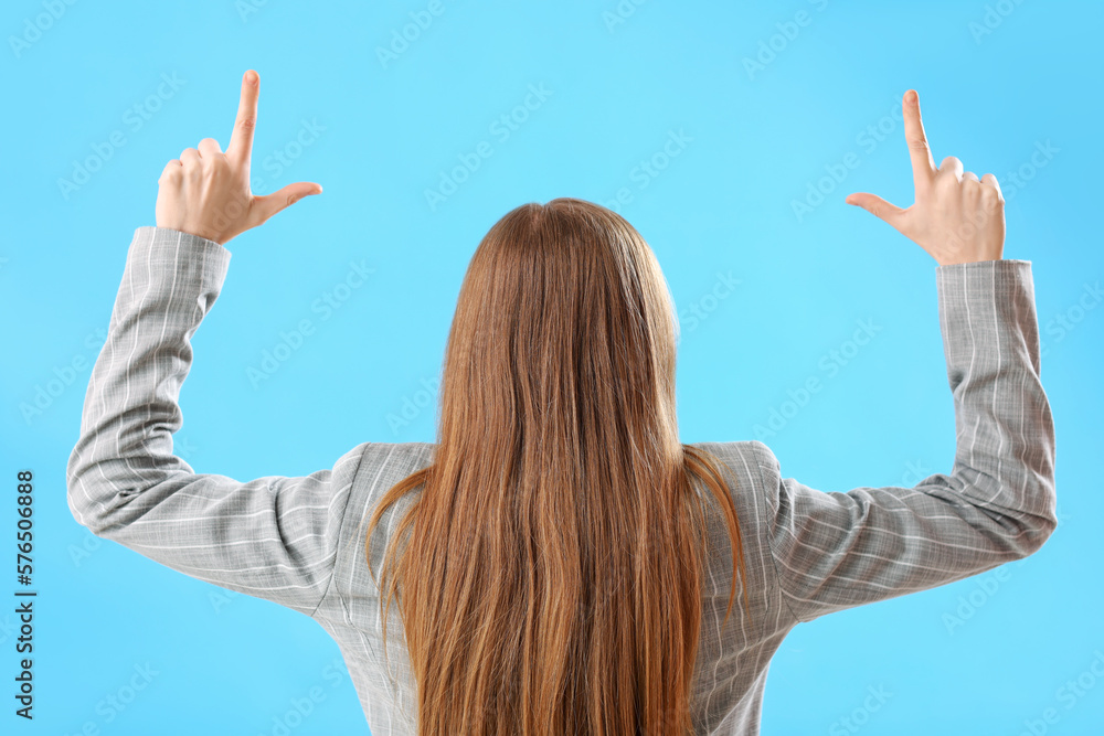 Young businesswoman showing loser gesture on blue background, back view